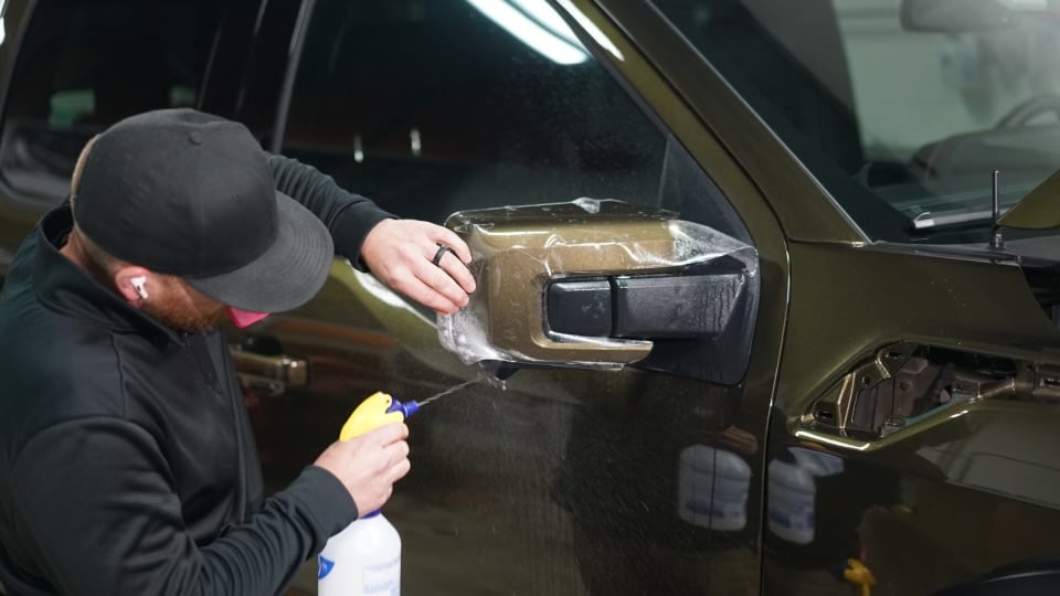 PPF being installed on a mirror by Tabula Rasa Fine auto Detailing, using a high end sprayer bottle - 2024 Ford Raptor